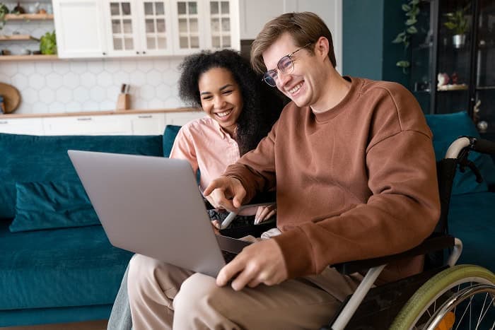 Person in wheelchair and support worker collaborating on laptop